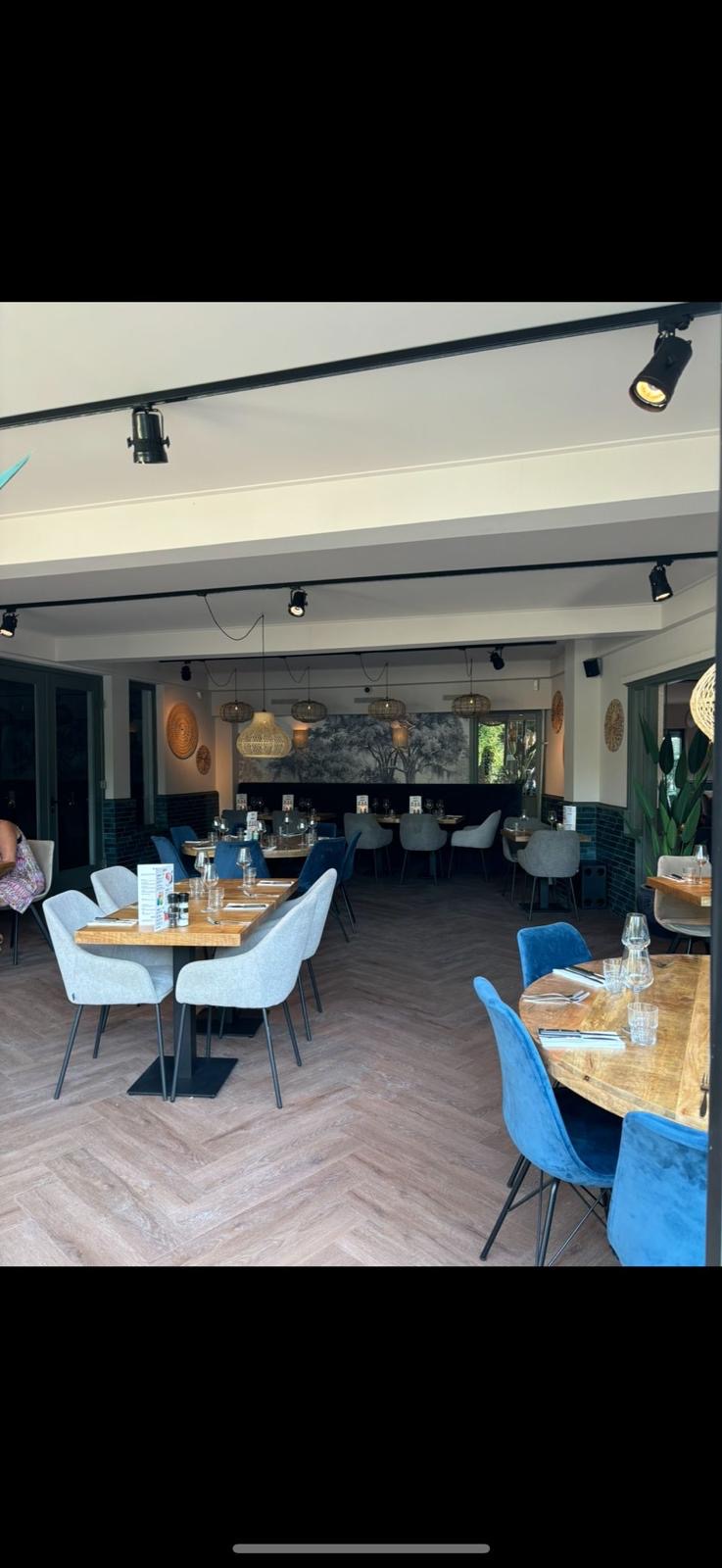 Verbouwd restaurant met visgraatvloer, blauwe stoelen en railverlichting