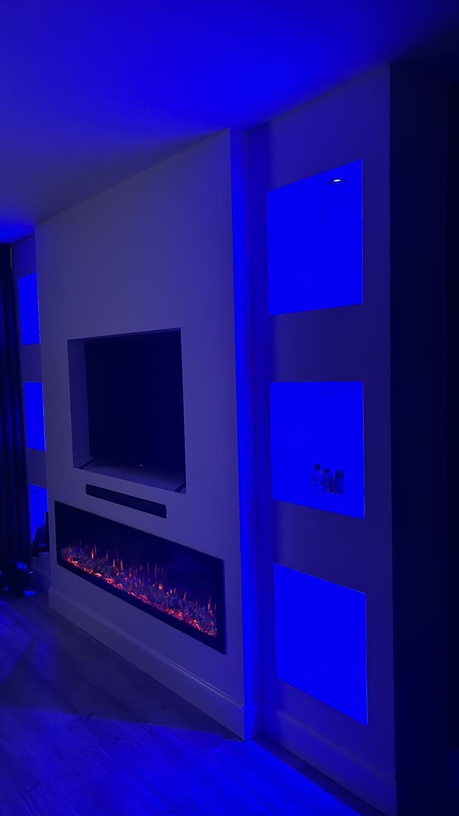 Maatwerk tv-wand met elektrische haard en nissen met blauwe sfeerverlichting