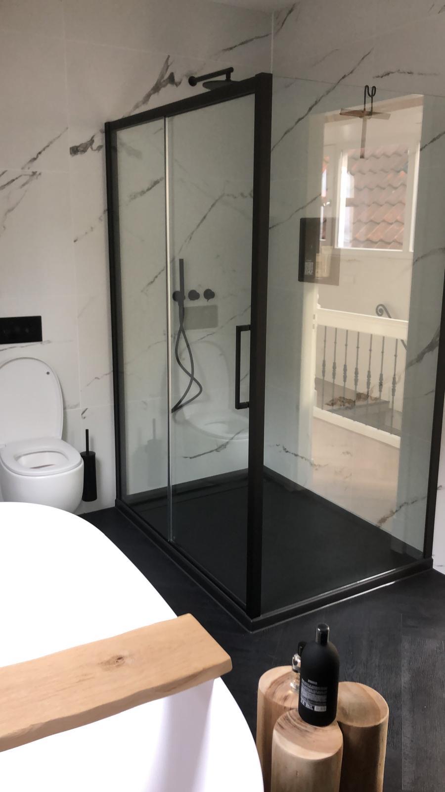 Moderne badkamer met marmerlook tegels, zwarte douchecabine en vrijstaand bad