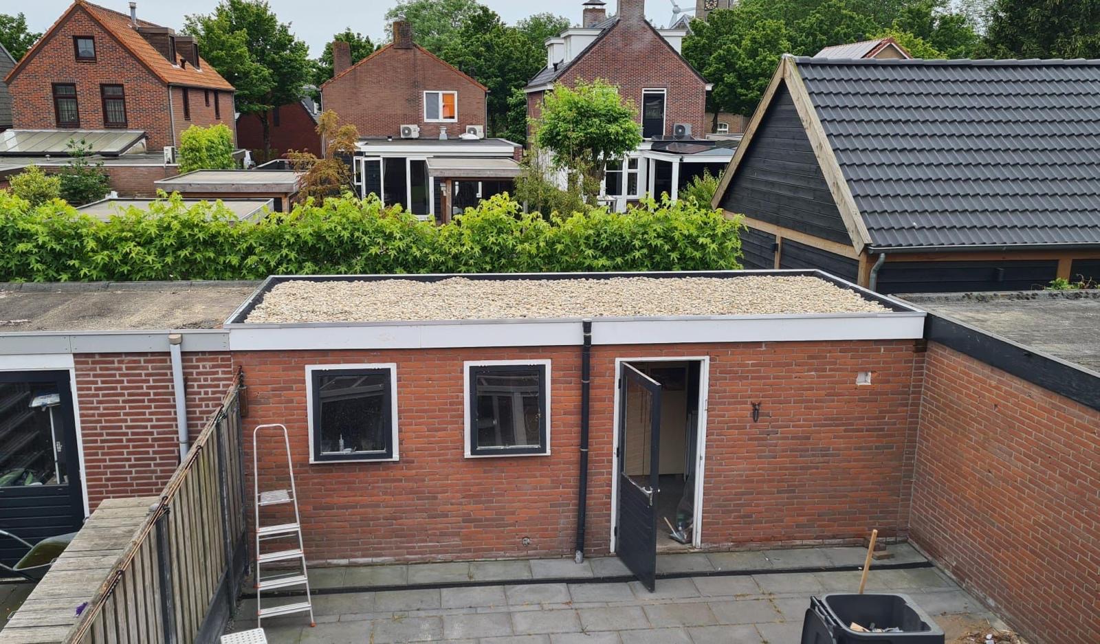 Plat dak van een bakstenen bijgebouw bedekt met grindballast en witte boeiboord